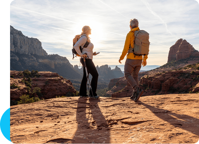 Two hikers enjoy a scenic view atop rocky cliffs during sunset.